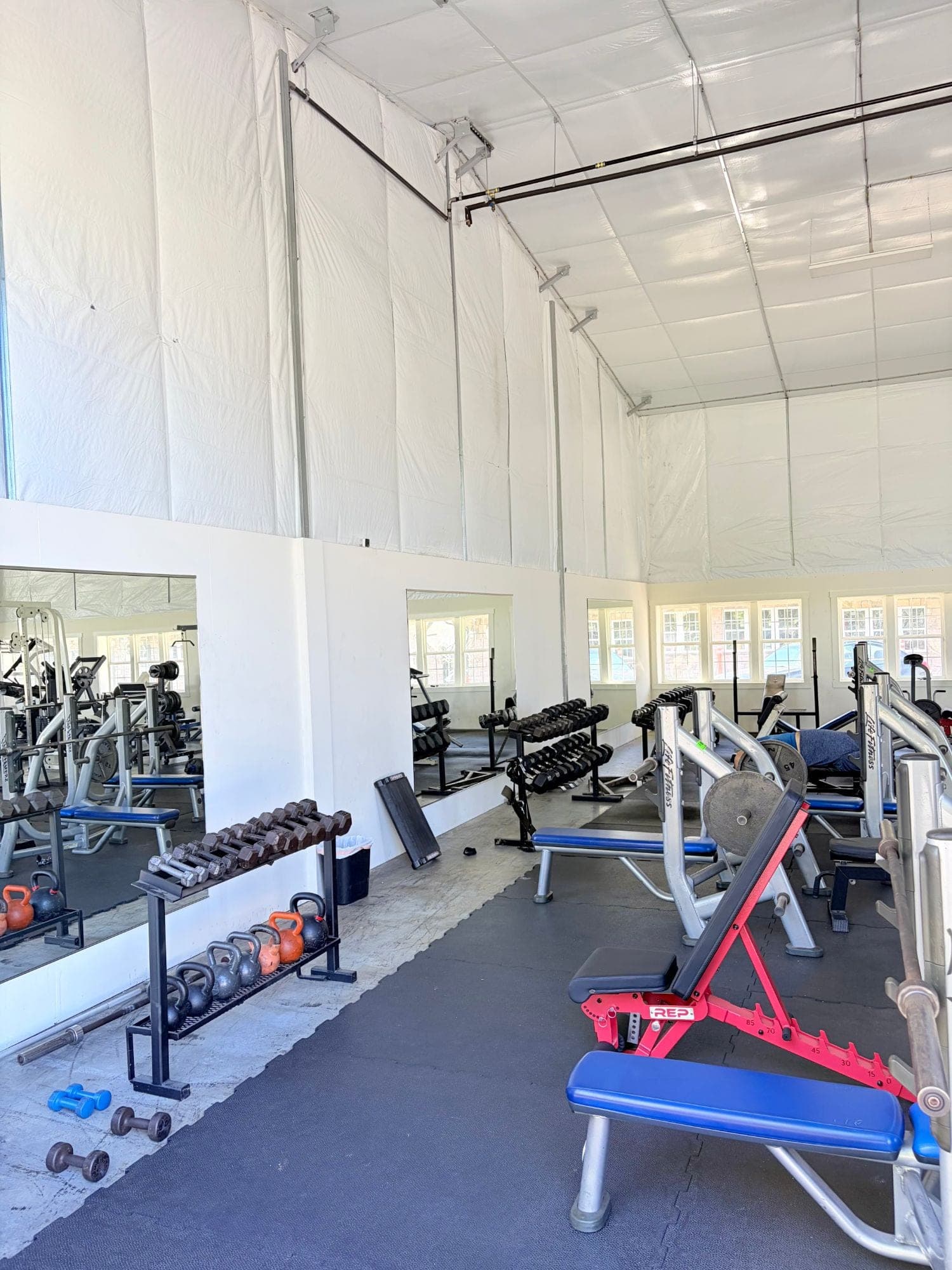 Free weight room with dumbbell racks, kettlebells, benches and mirrored walls