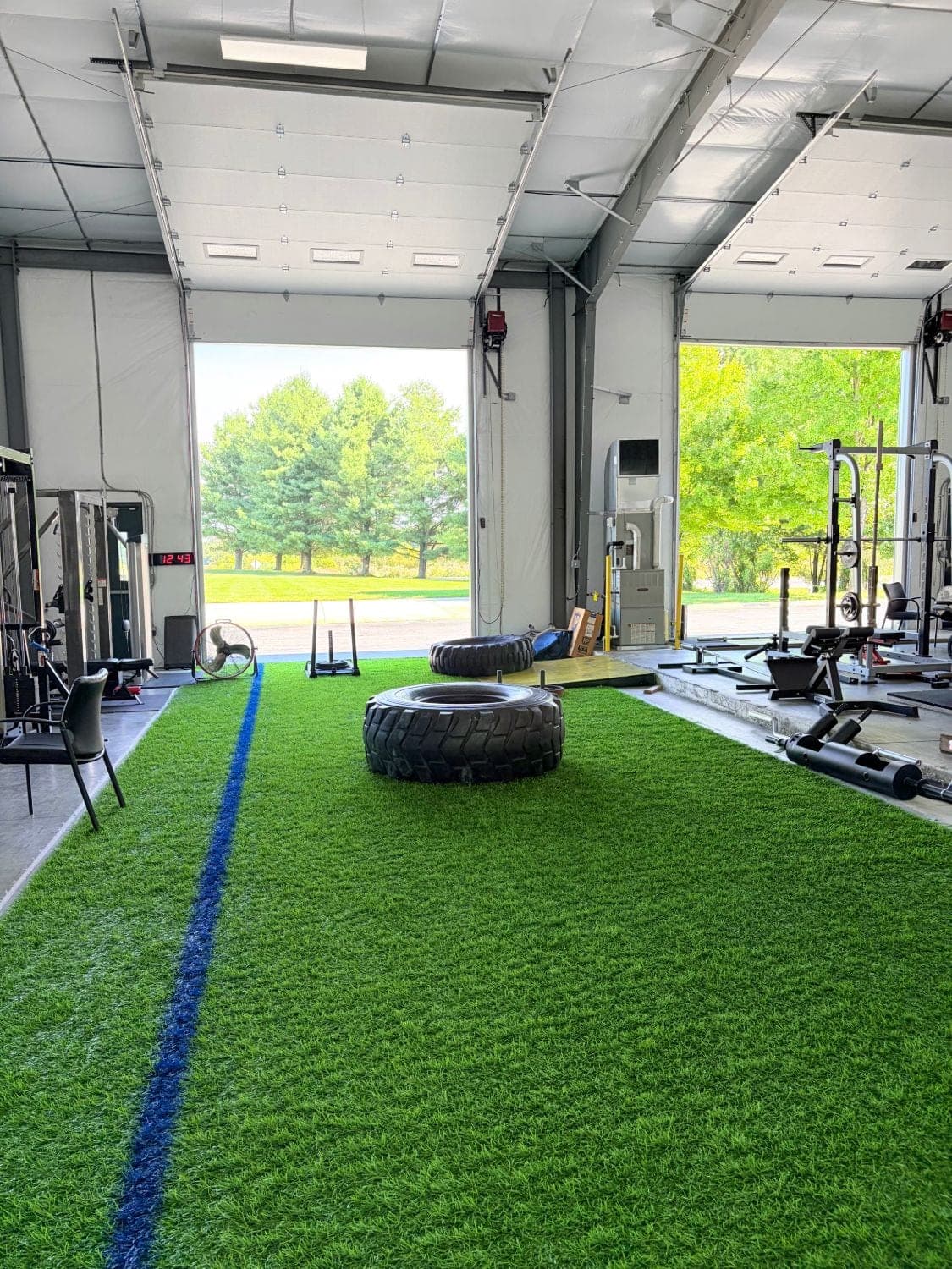 Turf run with tires and a sled, roll-up doors open to daylight